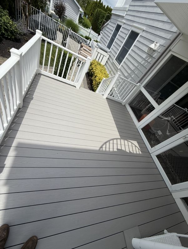 Deck boards and white railings running along the house, with the stairs down to the yard